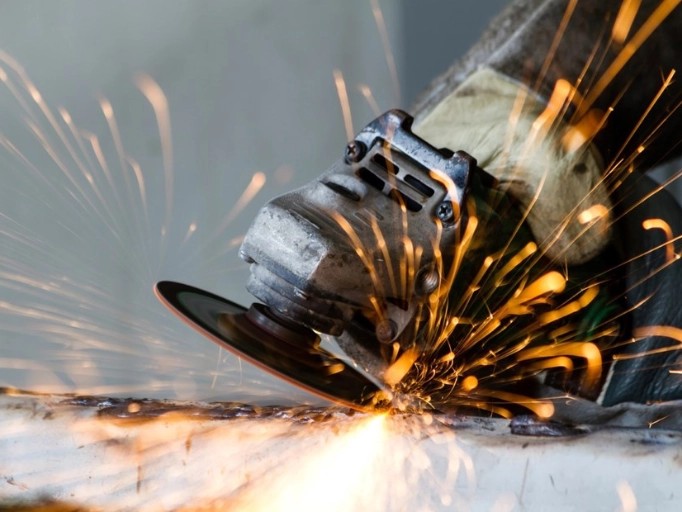 Mechanic using a cordless angle grinder on a car part