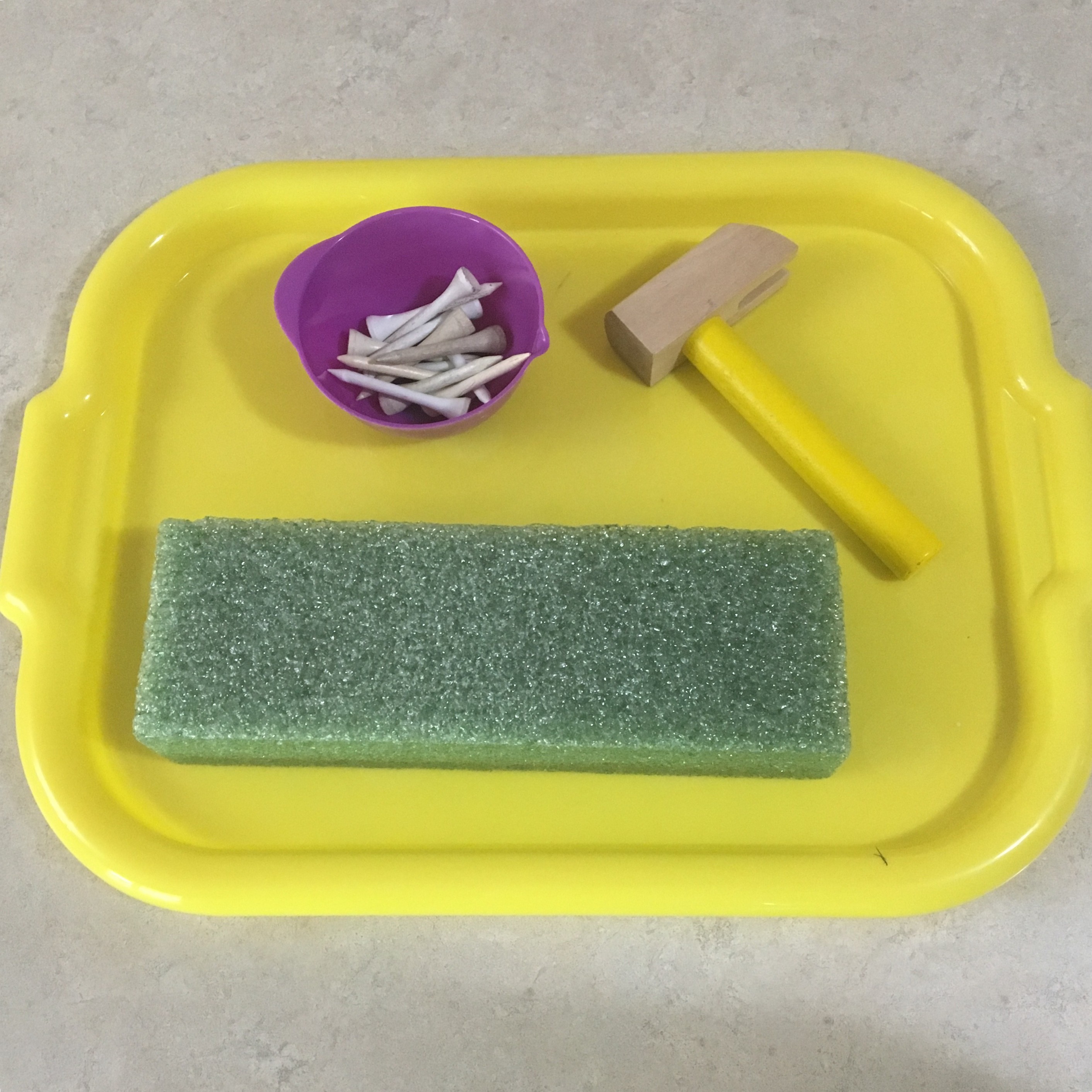 Toddler intently hammering golf tees into a foam block