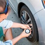 person checking tire pressure with manual gauge on a silver car