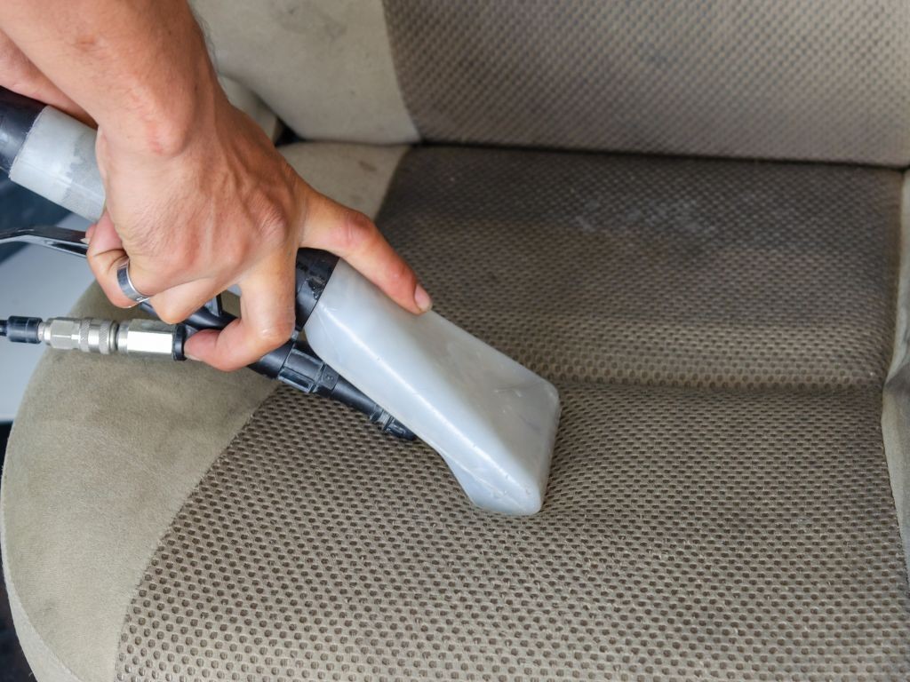 alt text: a person vacuuming dog hair from a car seat